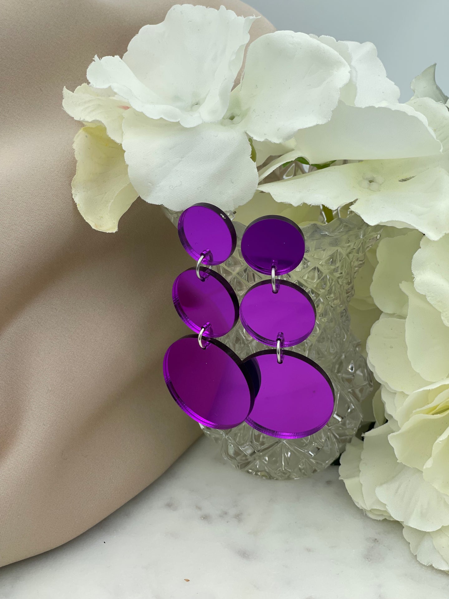 Kauniisti valoa heijastavat lilat peilikorvakorut.